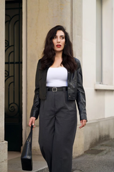 a lady in a white top, a black leather jacket and a pair of grey pants